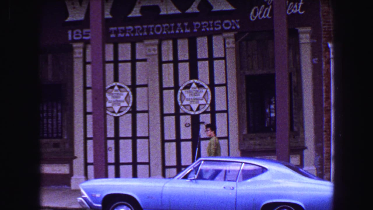 Man in a green shirt walks past a Territorial Prison facade behind a blue car.