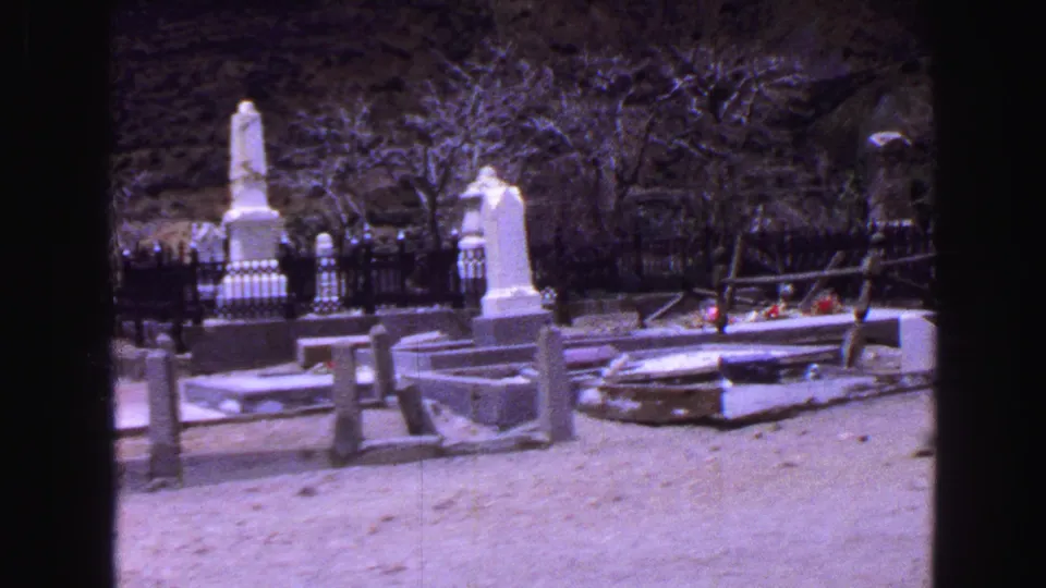 1968 Vancouver cemetery view with upright grave monuments, low railings, bare trees, and pale ground in a purple-tinted 8mm frame.