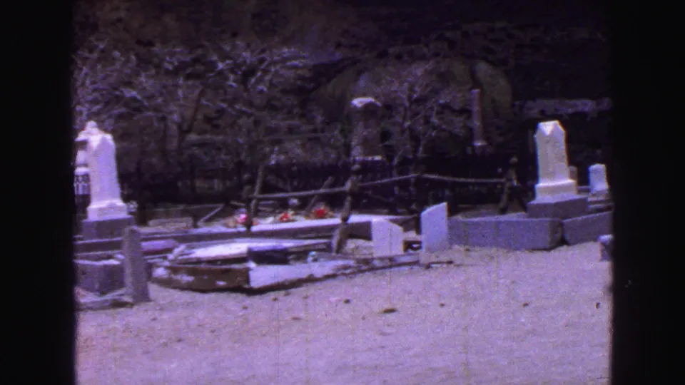 Purple-shifted 8mm frame of a 1968 Vancouver cemetery with flat grave slabs, upright markers, railings, and red flowers.