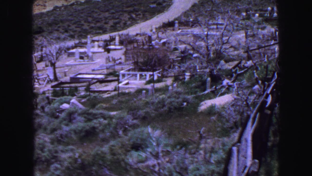 1968 Vancouver 8mm frame overlooking a hillside cemetery with winding paths, low markers, shrubs, and trees.