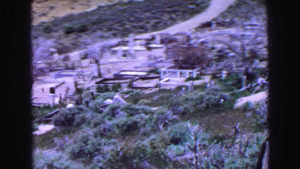 1968 Vancouver home-movie frame showing a cemetery landscape with paths, low memorials, trees, and hillside vegetation.