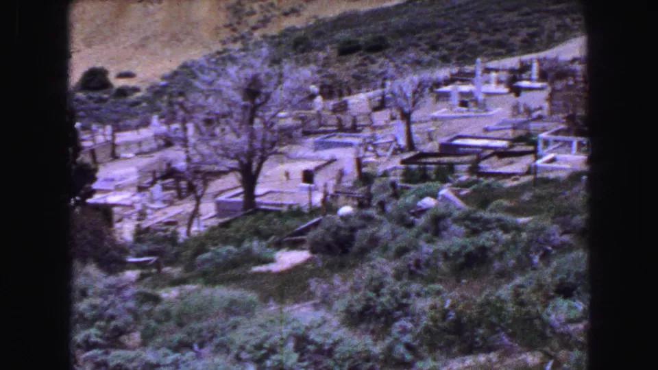 1968 Vancouver 8mm frame of a hillside cemetery with bare trees, pale paths, low monuments, and green foreground growth.