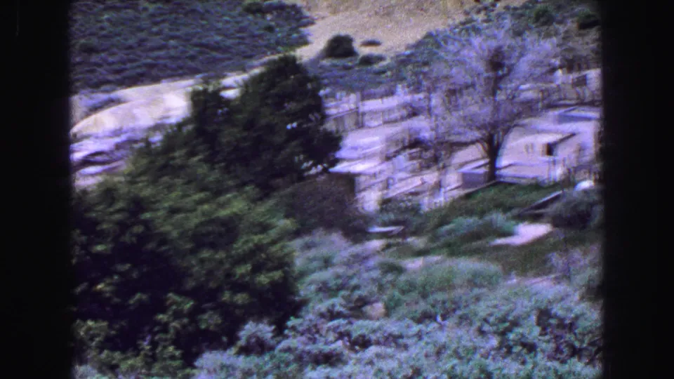 1968 Vancouver 8mm frame with motion blur during a pan across cemetery shrubs, trees, paths, and low memorial structures.