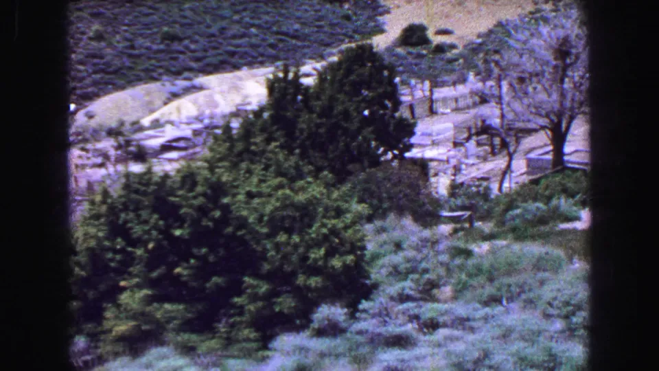 1968 8mm travel frame showing a scrubby hillside, trees, and a pale winding path in a Lake Tahoe area landscape, with no person clearly visible in this still.