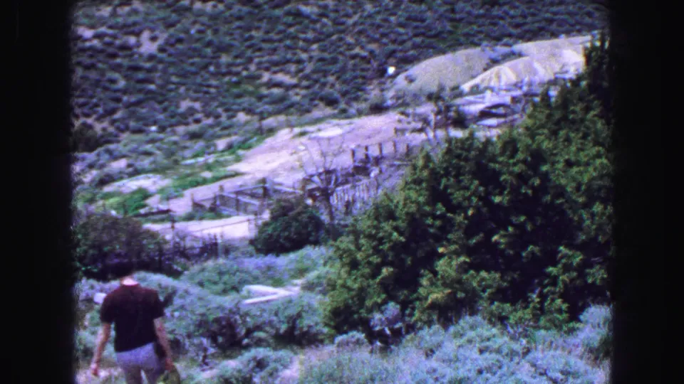 A distant adult in a short-sleeve top and shorts walks down a scrub-covered hillside during a 1968 8mm Lake Tahoe travel scene.