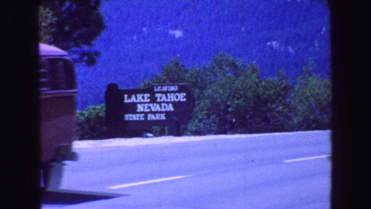The Lake Tahoe Nevada State Park sign stands beside the highway with trees and bright blue sky behind it.