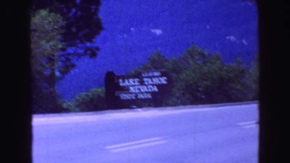 A slightly blurred 8mm view shows the Lake Tahoe Nevada State Park sign across the highway with trees behind it.