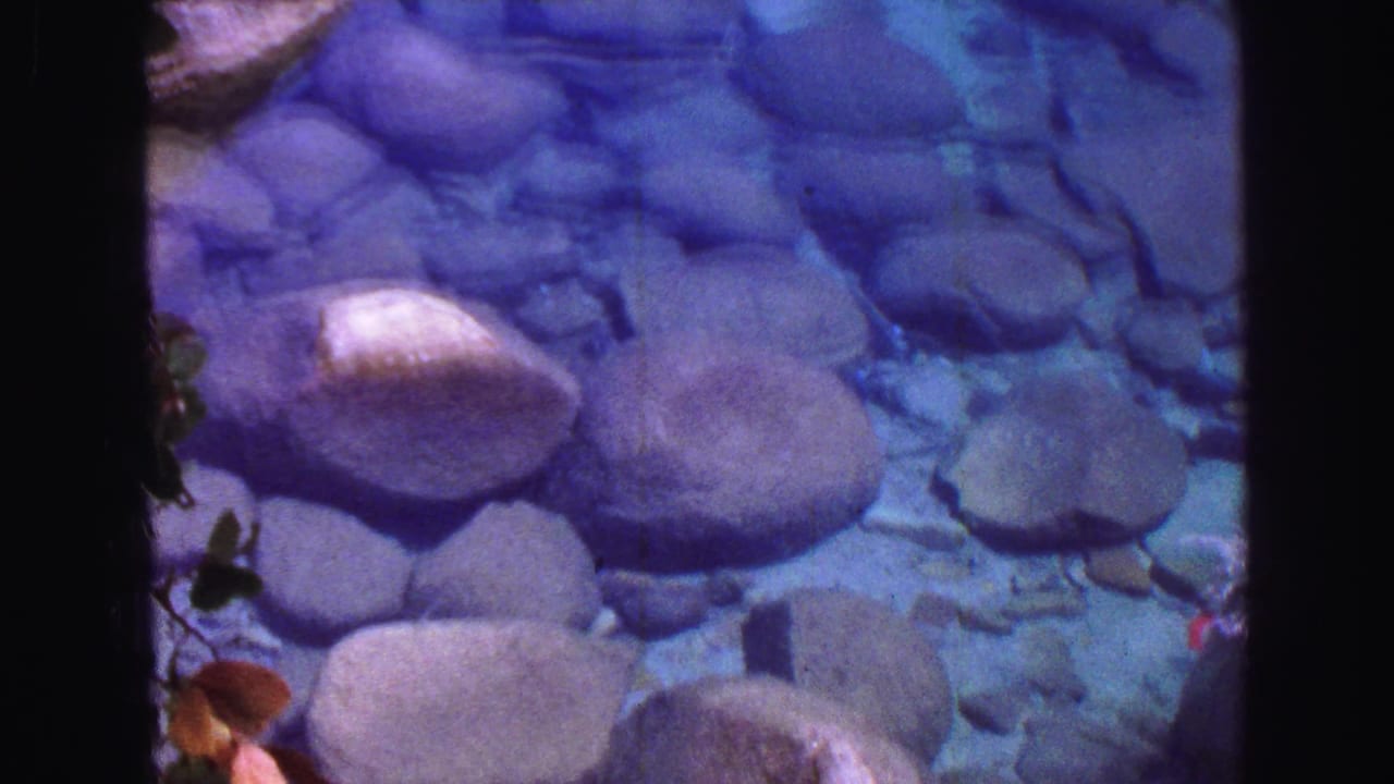 Clear water flowing over rounded river stones with dark film-frame borders.