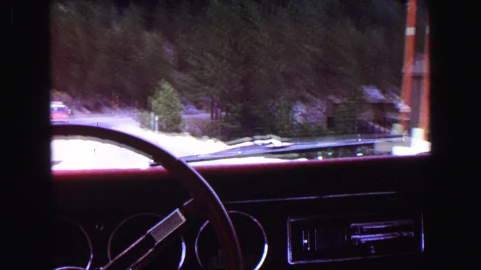 Final 1968 in-car frame shows the road, evergreens, utility pole, and lodge-like building passing through the windshield.