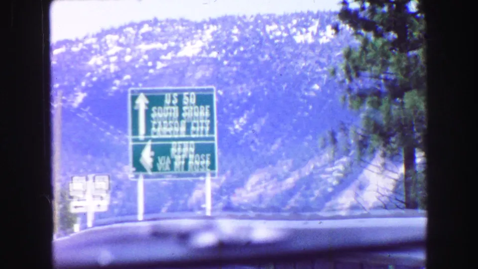 Green U.S. 50 guide sign listing South Shore, Carson City, and Reno, seen from a classic car on a mountain road in 1968 footage.