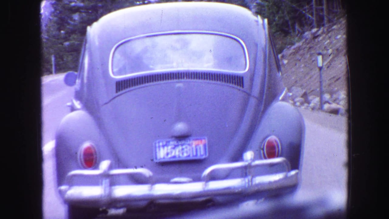 1968 Vancouver-area home-movie frame of a blue Volkswagen Beetle with chrome bumper traveling ahead on a rural road.