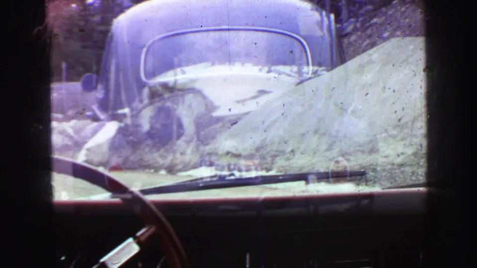 1968 Vancouver-area 8mm frame with the Beetle ahead, seen through a following car windshield with dashboard and wiper visible.