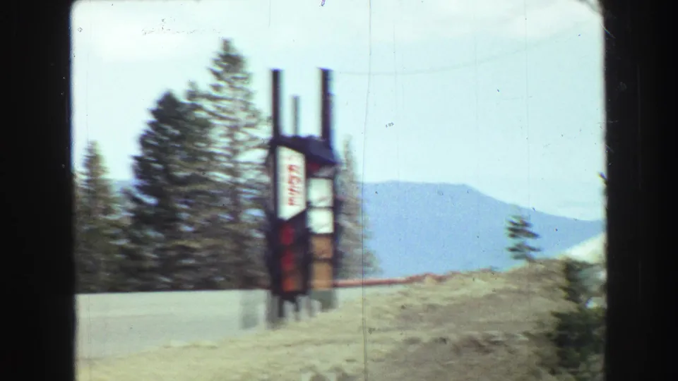 1968 Vancouver-area 8mm frame showing a blurred roadside sign, evergreens, and distant mountains during travel.
