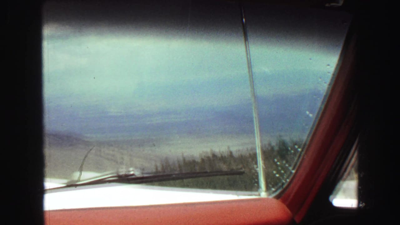 View through a windshield with red dashboard, wipers, trees, and hazy mountains.