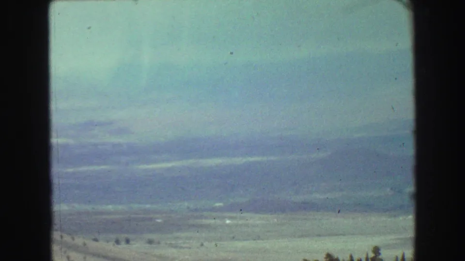 Faded 8mm view of open terrain and distant mountains through a car window during a 1968 British Columbia road trip.
