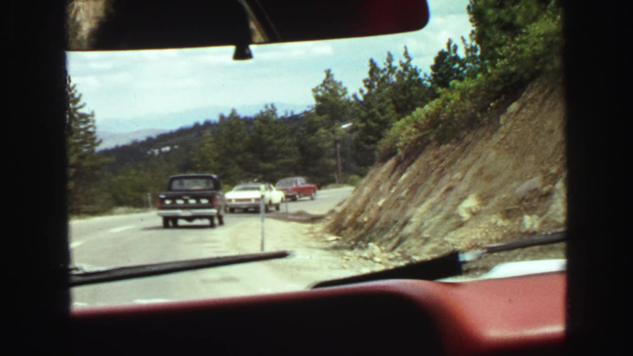 View through a car windshield of older vehicles on a winding mountain road.