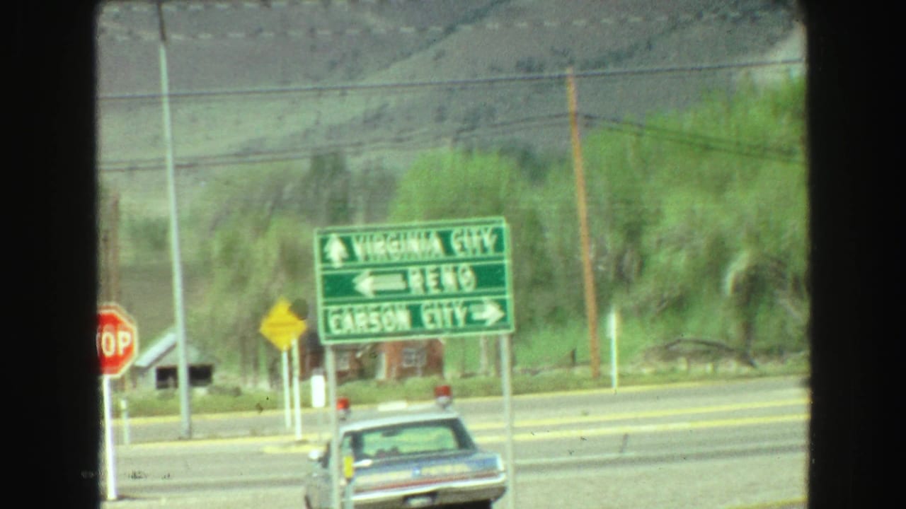 Green directional road signs, stop sign, sedan, utility poles, and rural hills near a highway.