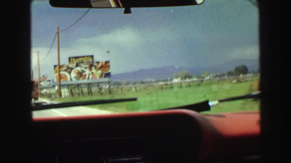 1968 car-window view of a Harrah's billboard beside an open field, with mountains or hills in the distance and a wiper in foreground.