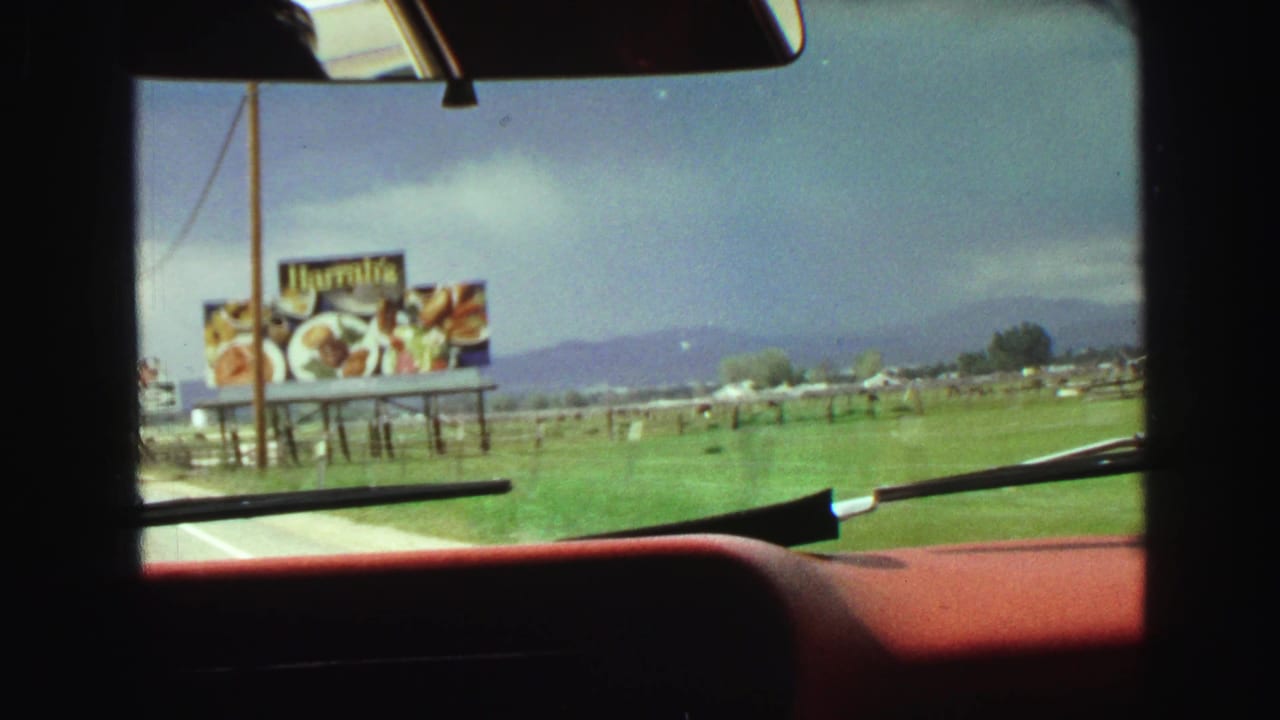 View through a car windshield toward a Harrah's food billboard beside open fields.