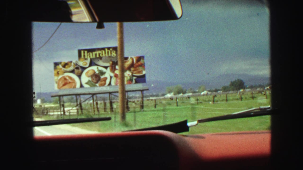 Car windshield view with a large Harrah's billboard closer to the roadside.