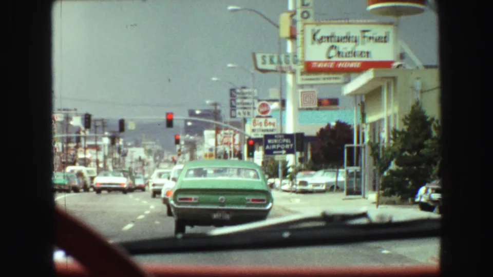 1968 Vancouver street scene from inside a moving car, showing traffic, storefront signs, and a Kentucky Fried Chicken restaurant sign.