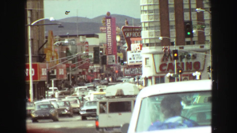 1968 Vancouver downtown street with heavy traffic, vertical signs, traffic signals, and hills visible beyond the buildings.