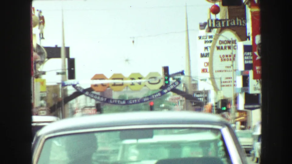 1968 8mm view down a commercial street with traffic, vertical signs, and an arch that appears to include Reno lettering.