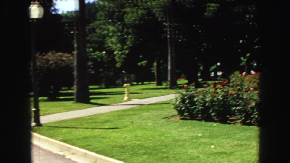 1968 Vancouver park view showing lawn, a sidewalk, lampposts, trees, and a yellow post near the walkway.