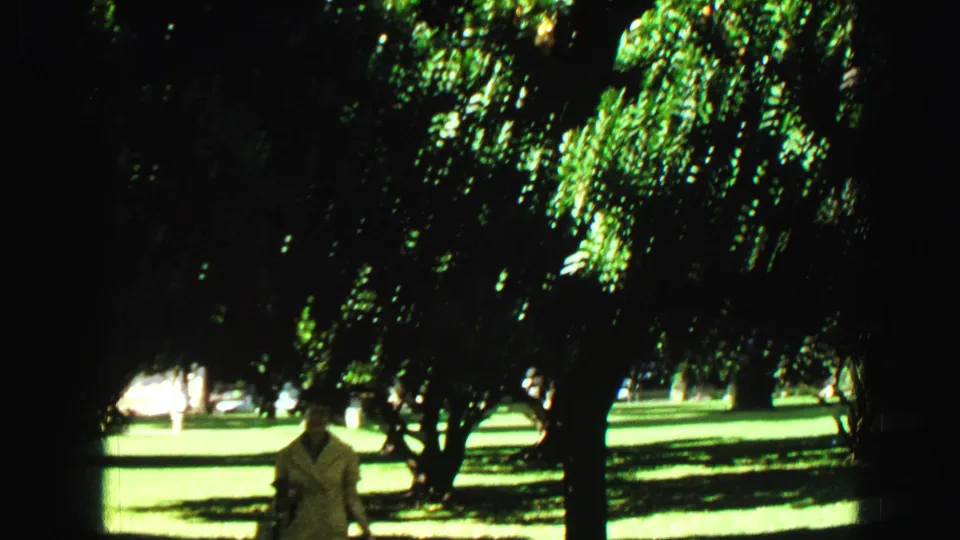 A woman in a light dress appears near the lower frame as trees and bright lawns fill the Vancouver garden scene.