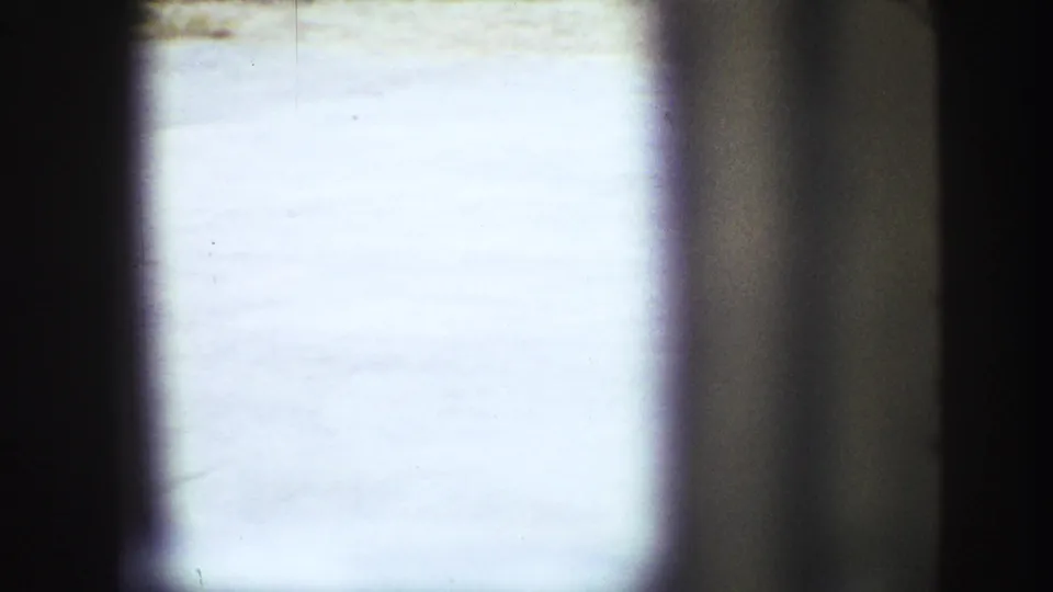 1968 Vancouver home-movie view toward a pale paved yard surface, framed by dark edges and a blurred vertical foreground shape.