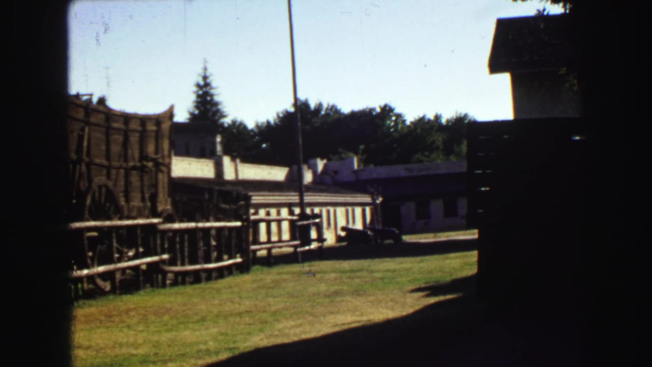 Visitor-shot 8mm frame showing the wagon, fence and buildings at the Sutter's Fort site under bright sun.