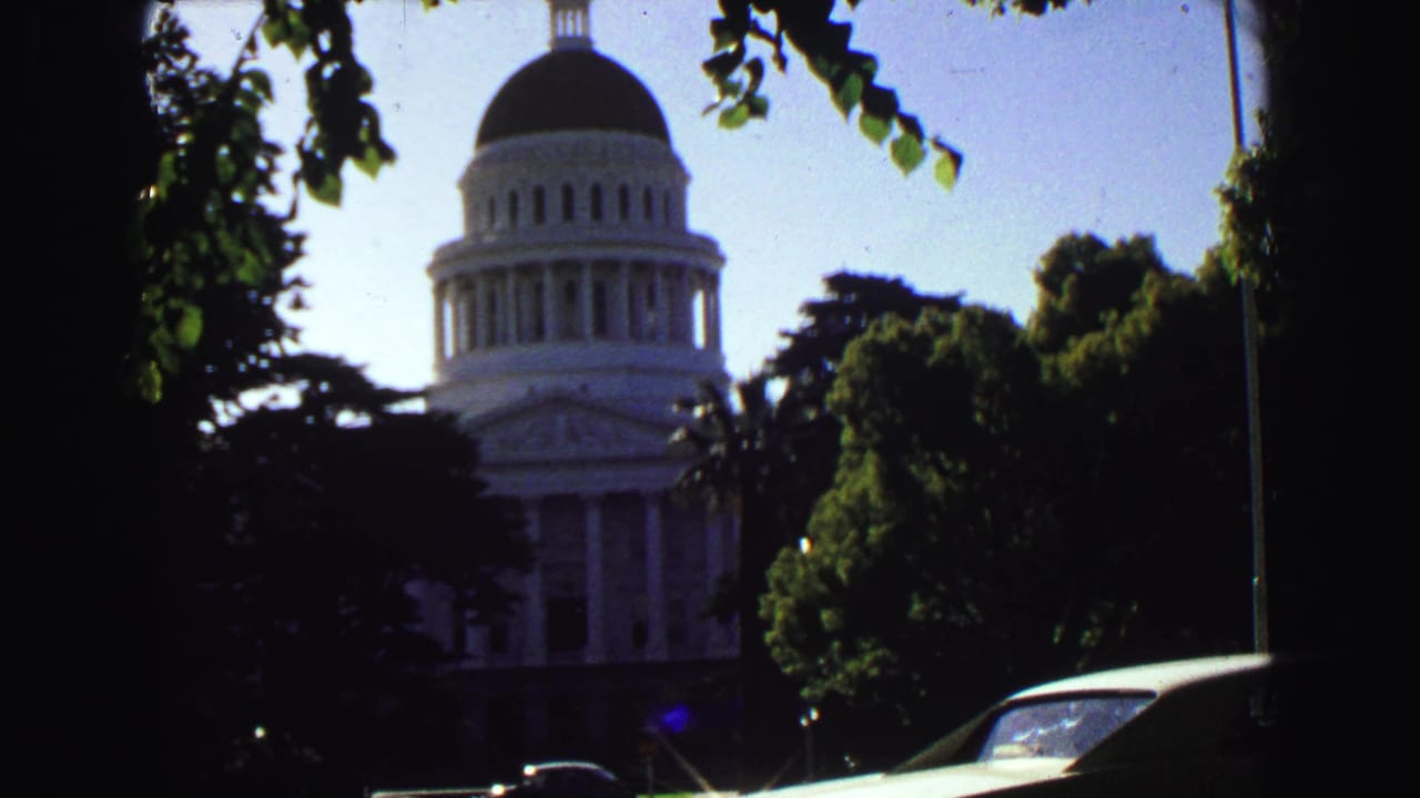 White domed civic building partly framed by trees, with cars in the foreground.