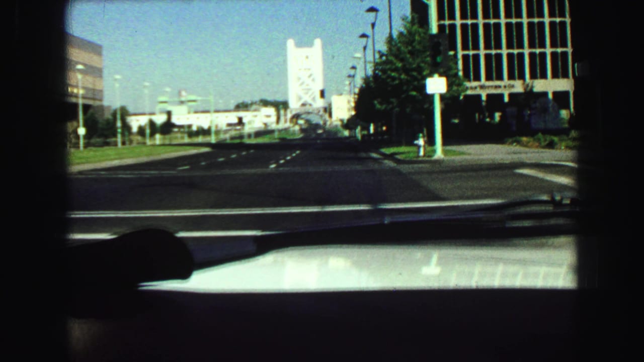View through a car windshield toward a broad city street and distant bridge structure.