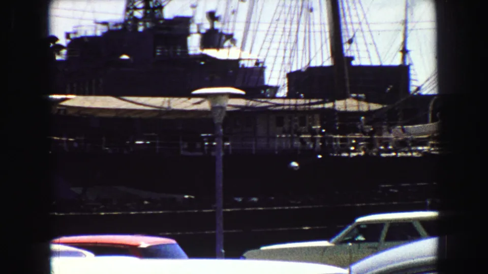 Vancouver waterfront frame showing rigging, dark ship forms, a railing, and period cars parked in the foreground.