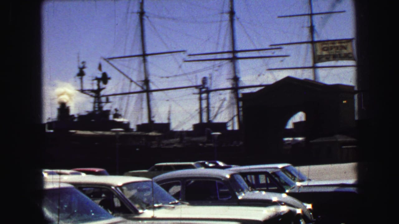 Harbor parking lot with classic cars, boat masts, a dark pier structure, and a visible sign.