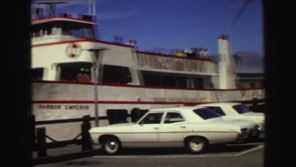 1968 Vancouver home-movie frame showing a white passenger ferry docked beside classic sedans near a pier.