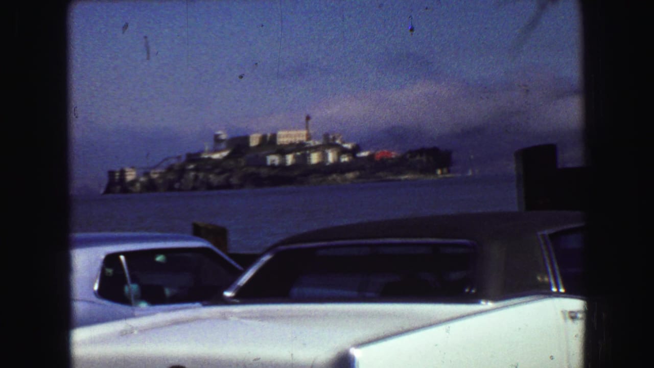 1968 8mm view toward Alcatraz Island across San Francisco Bay, with late-1960s cars parked along the waterfront.