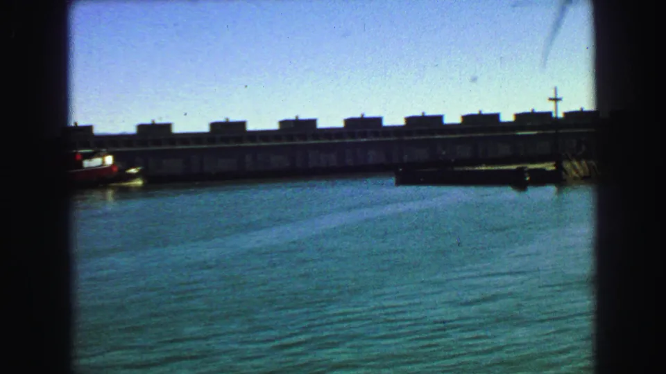 1968 8mm frame of San Francisco Bay water and a long waterfront pier, with a small boat near the structure.