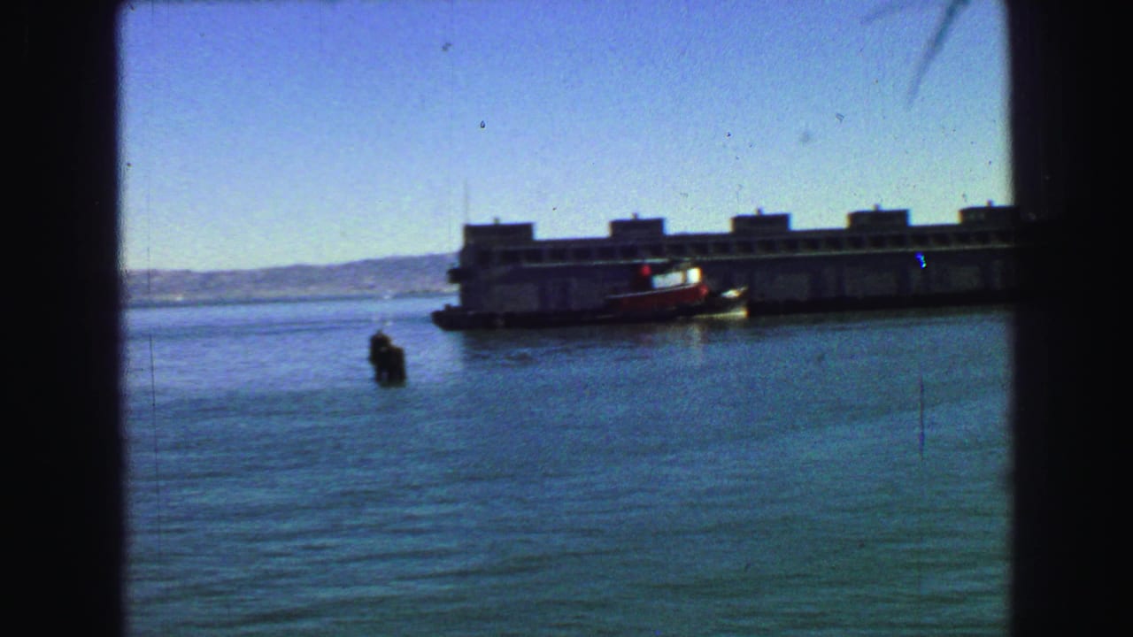Large vessel on calm water seen through dark window framing, with distant hills behind it.