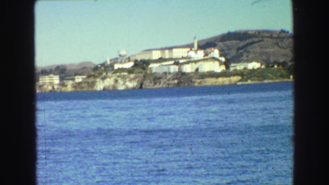 Bay water with an island shoreline and buildings seen from a boat through dark film borders.