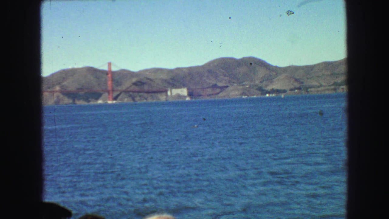 Distant Golden Gate Bridge across blue bay water with hills behind it.