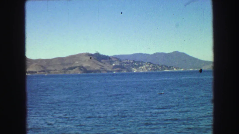 1968 8mm waterfront view across blue bay water toward distant hills and a small shoreline settlement near the Golden Gate area.