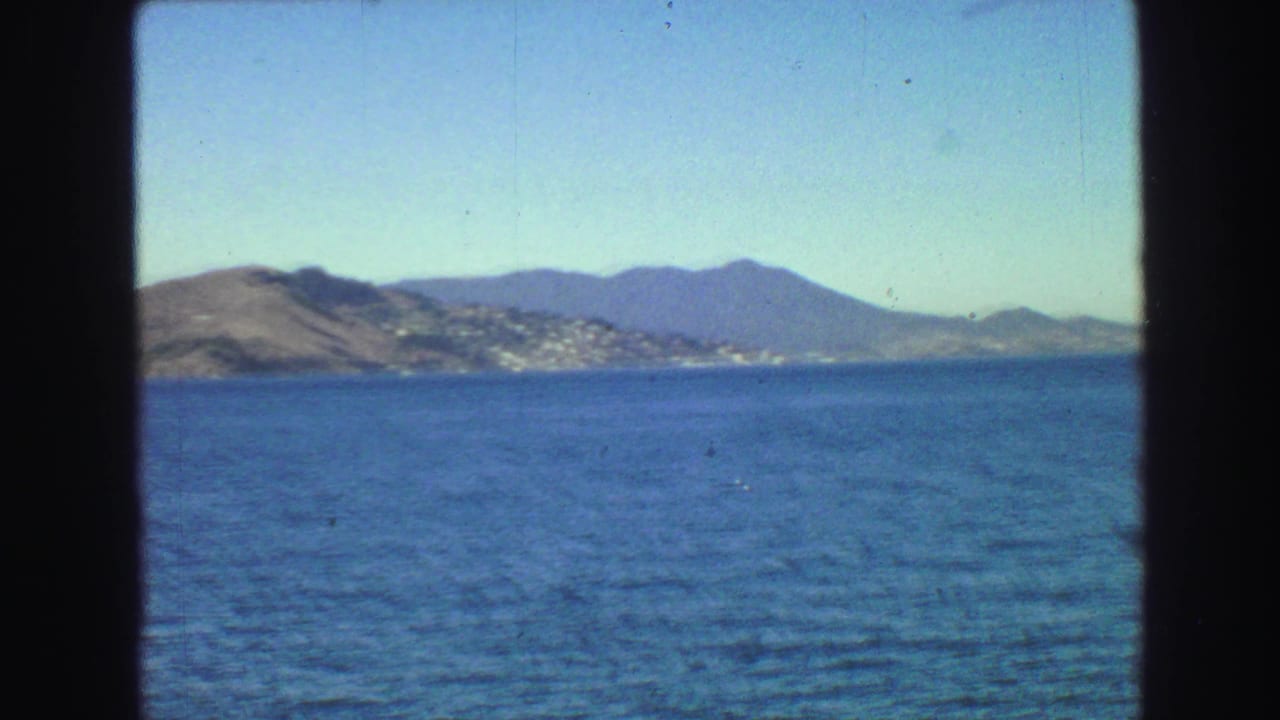 Blue water seen through dark boat-window edges with distant hills and shoreline under a clear sky.