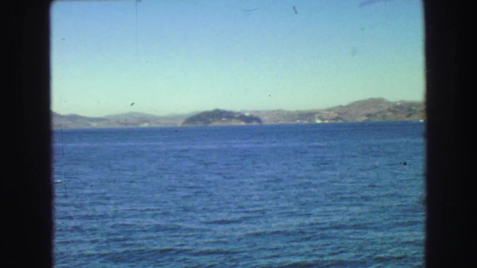 1968 Vancouver-area 8mm frame showing a broad water surface, low distant shoreline, and hills beyond the boat window.