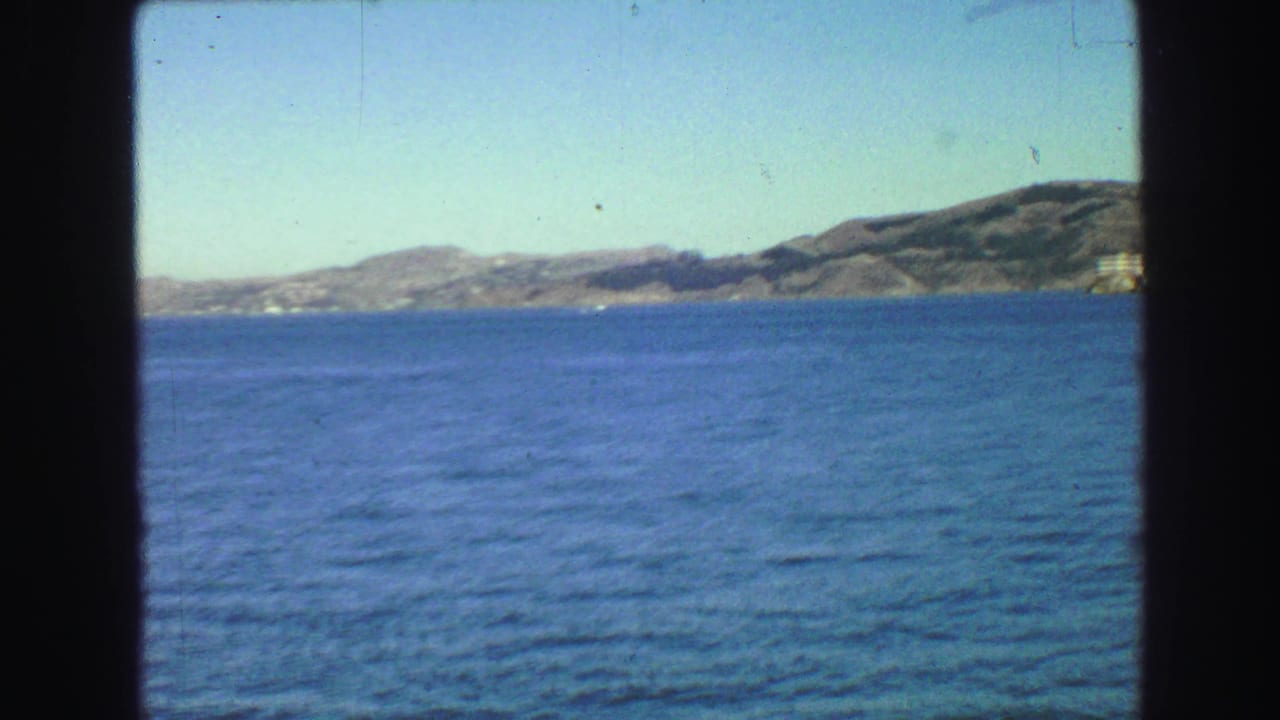 Blue bay water with low hills and distant shoreline under a pale sky.