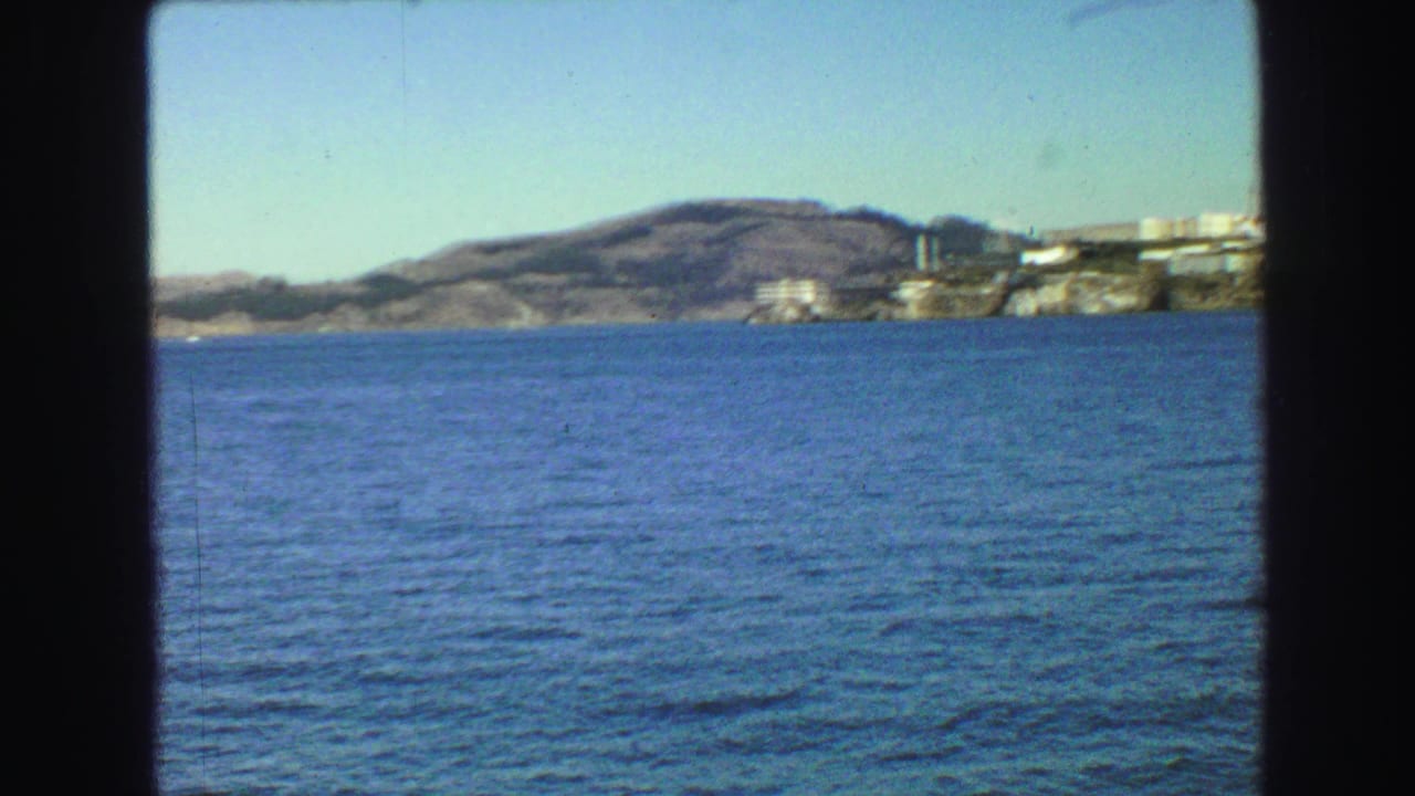 Open blue water with hilly shoreline and distant light-colored buildings.