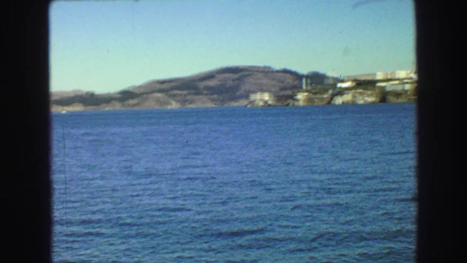 1968 8mm frame from a moving boat near Vancouver, with calm bay water, hills, and distant waterfront buildings.