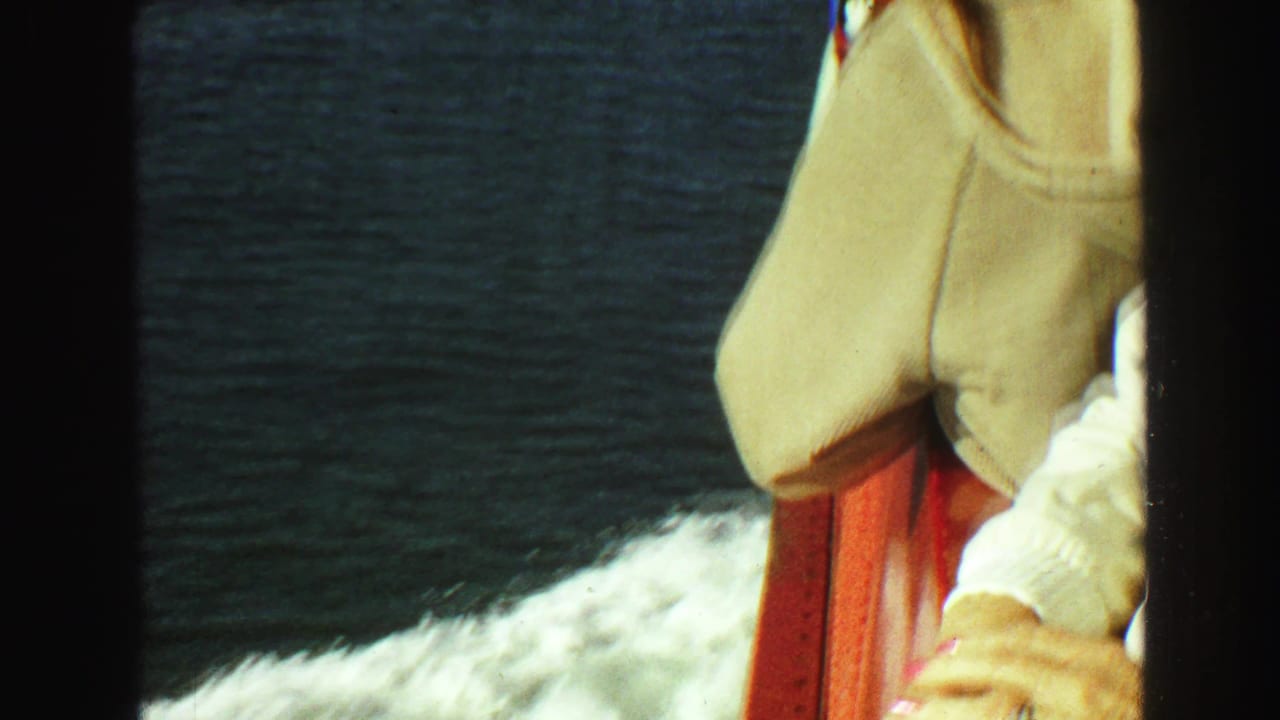 Partial view of a woman in a beige jacket by a red railing with water behind her.