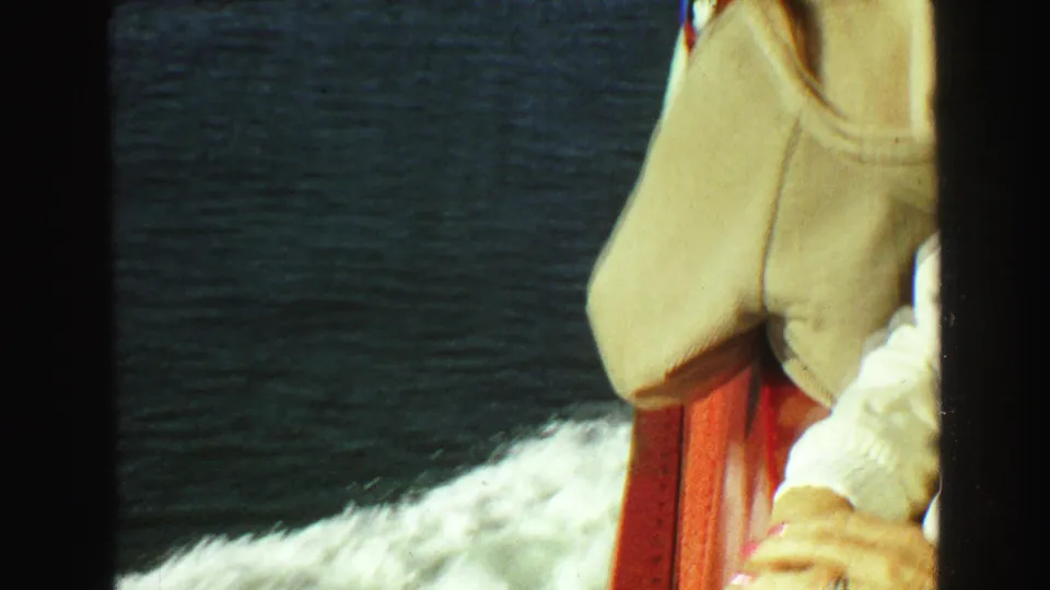 A woman in a beige jacket stands at a red ship railing against dark water in this 1968 Vancouver travel frame.