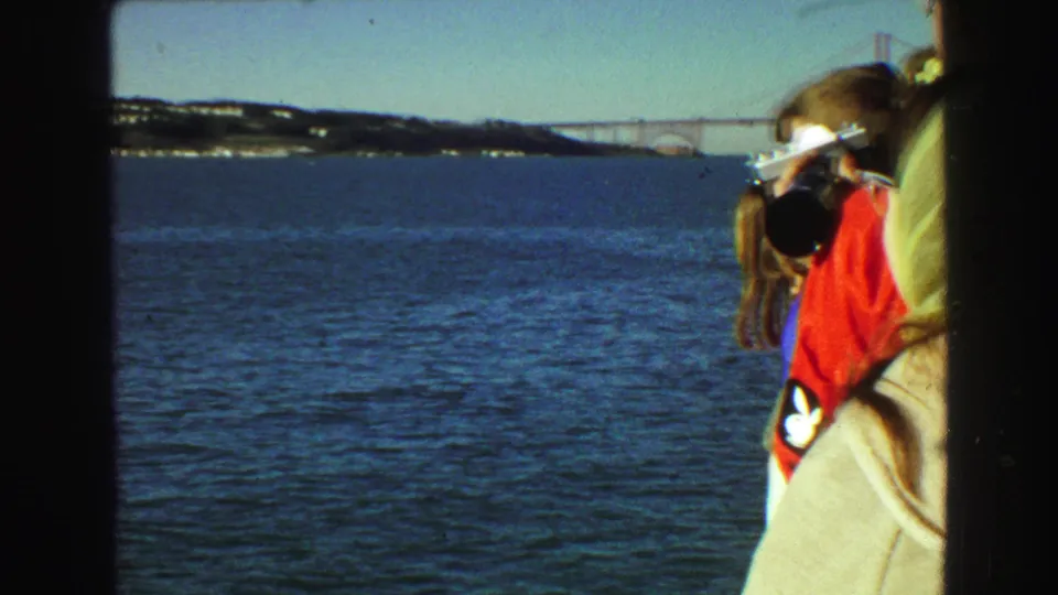 A 1968 Vancouver shipboard view shows a woman by the red railing, blue water, shoreline, and a distant bridge.